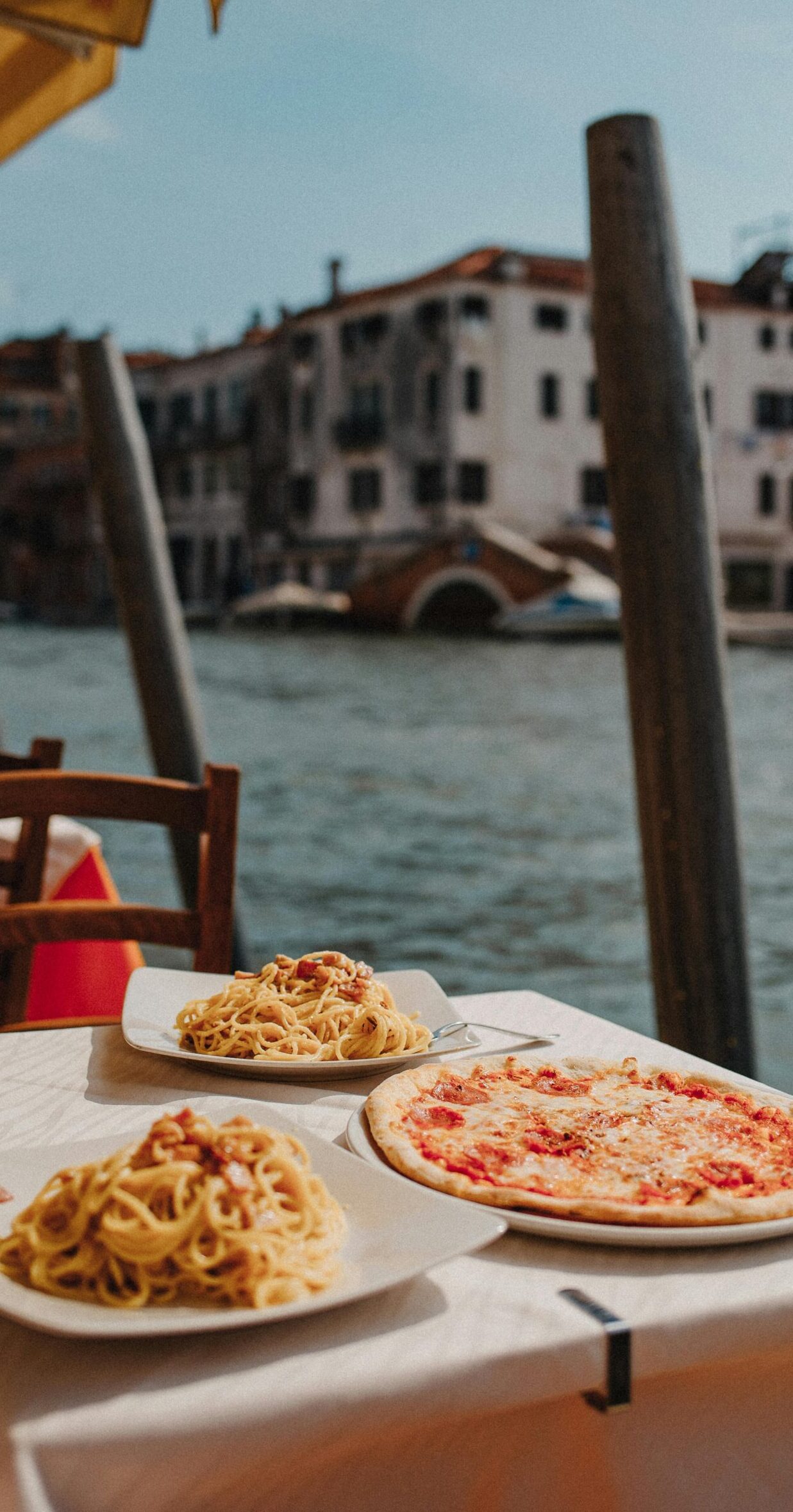 Delightful Italian pasta and pizza served by the scenic Venetian canal under sunny skies.